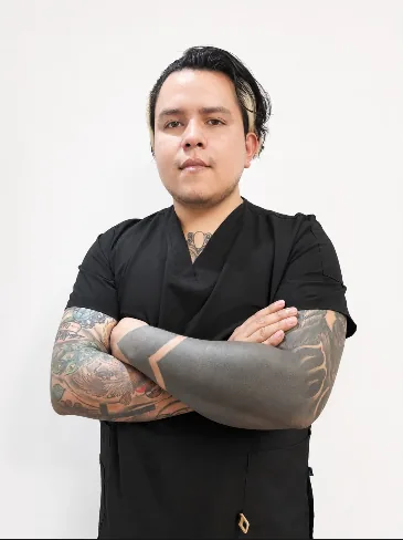 Retrato profesional del Dr. Alexis Fernández con uniforme quirúrgico negro y brazos cruzados